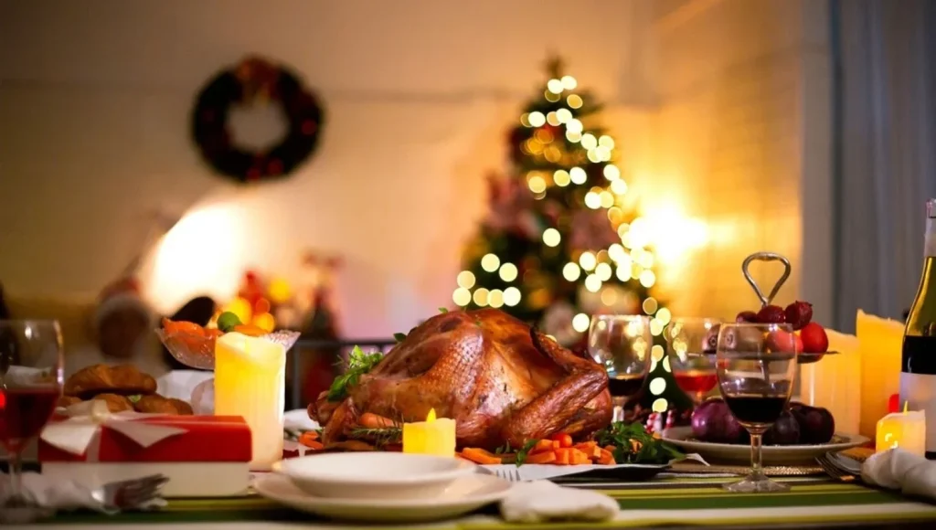 A festive table set for Christmas dinner with roast turkey, candles, and a tree in the background.